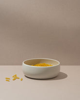 A white stoneware serving bowl with a simple design filled with yellow pasta. The bowl is placed on a neutral background.